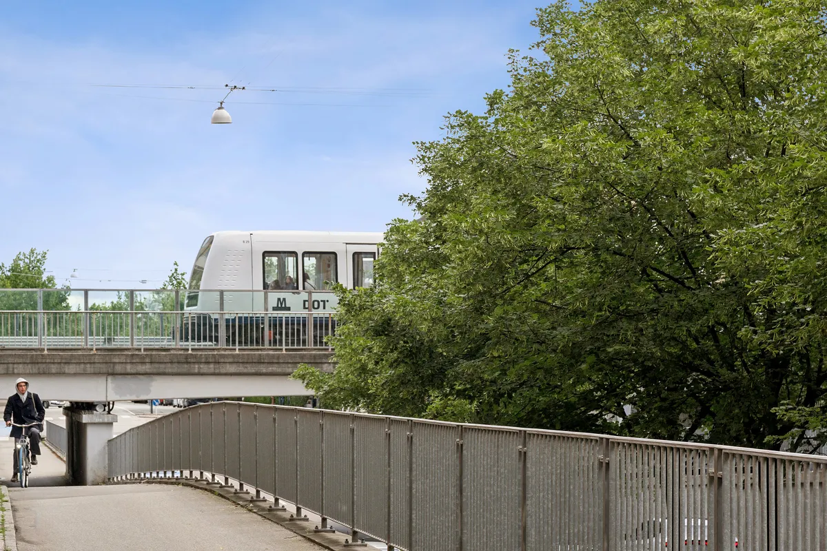 En cykelrytter kører gennem en stærk metalgitter-bro, der er forbundet med en jernbanebro, og der er en hvid metrovogn i afstand