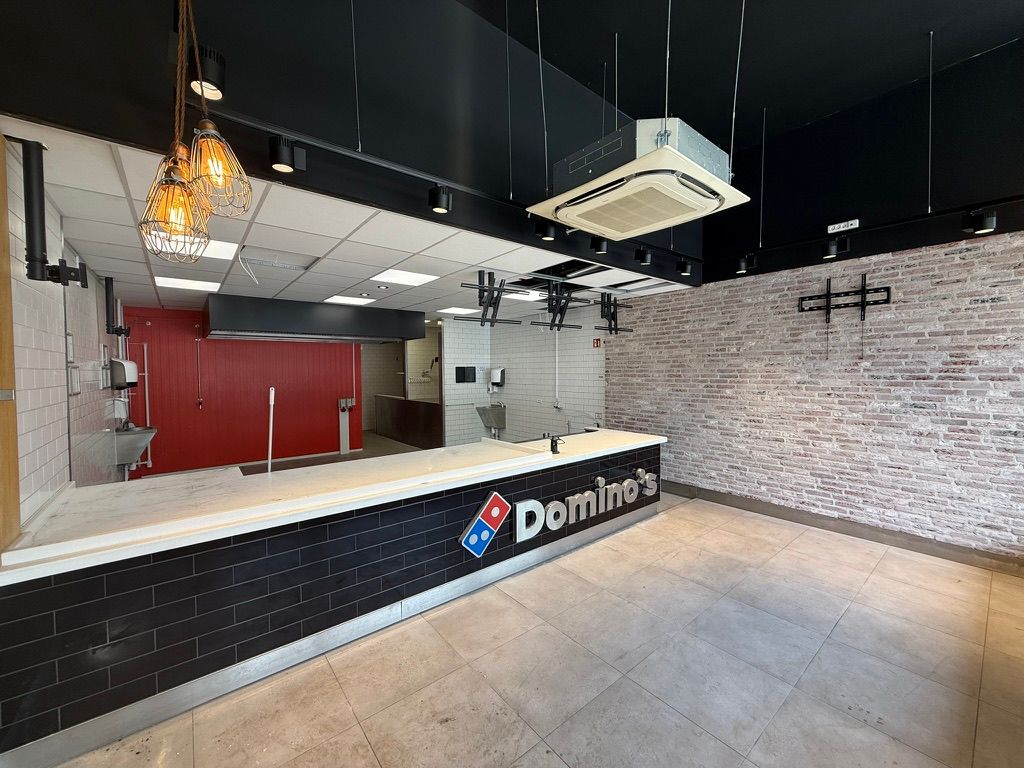 Take away-lejemål med dominos-logo, lyse gulve, højt loft, lyse loftslamper, røde vægge og søjler med hængelampe