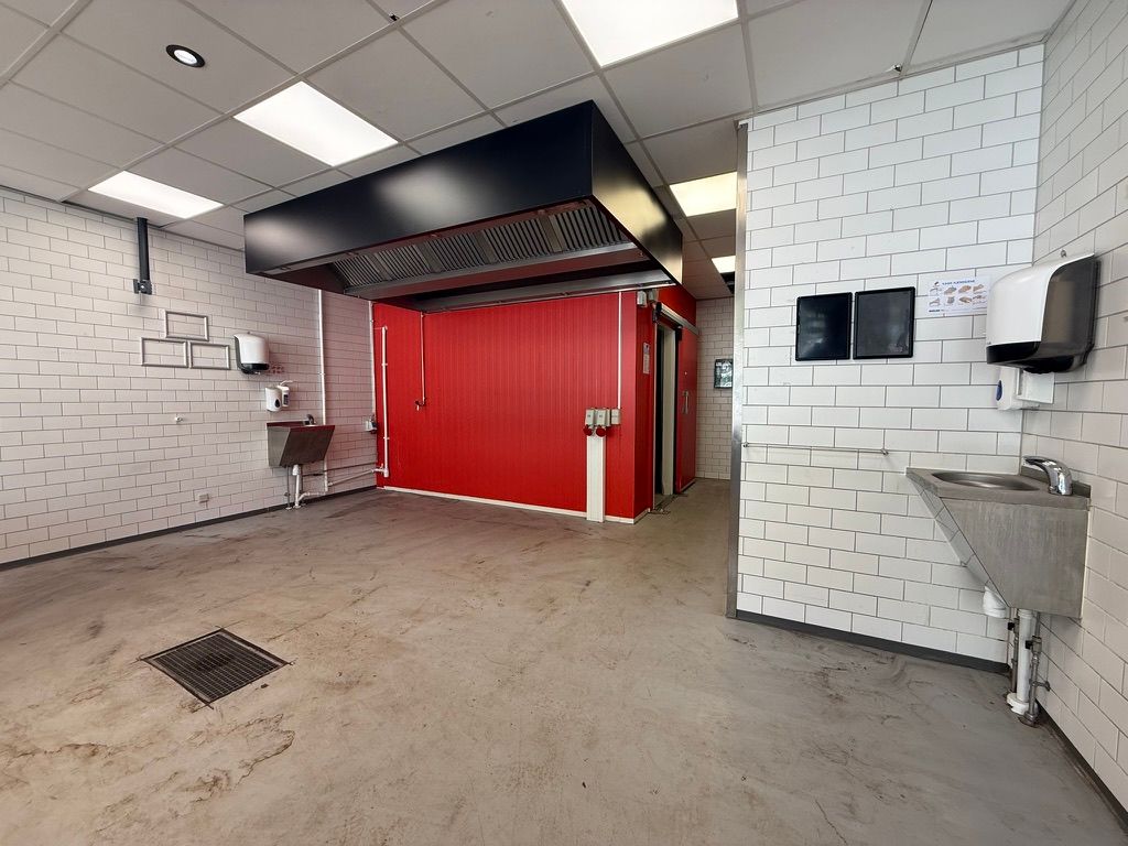 Take away-lokaler med rødt kølerskab og slibestensgulv og hvidt klinkerede vægge og loft