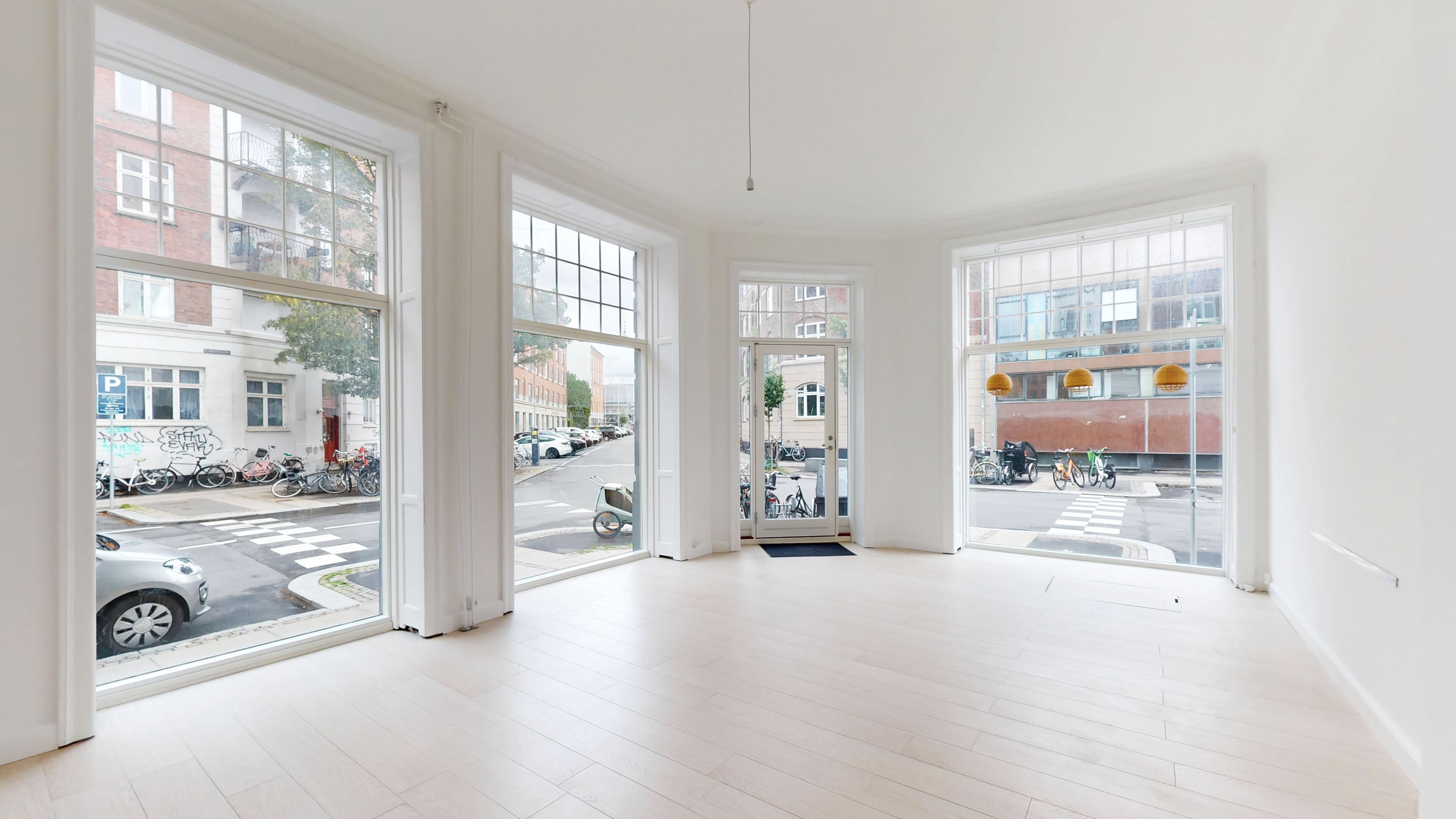 Moderne og ren designet butik med hjørnebeliggenhed og store vinduer. Ingen møbler og indretning. Solrigt med udsigt til parkeringsplads med biler og cykler.