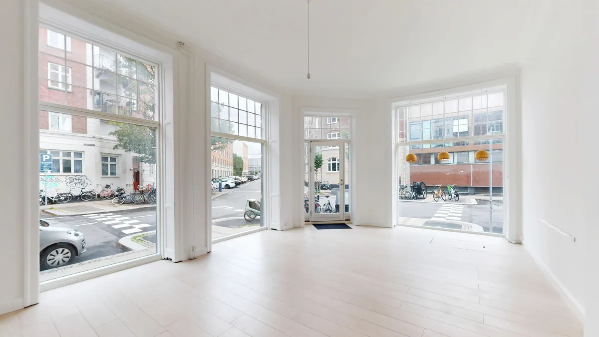 Moderne og ren designet butik med hjørnebeliggenhed og store vinduer. Ingen møbler og indretning. Solrigt med udsigt til parkeringsplads med biler og cykler.