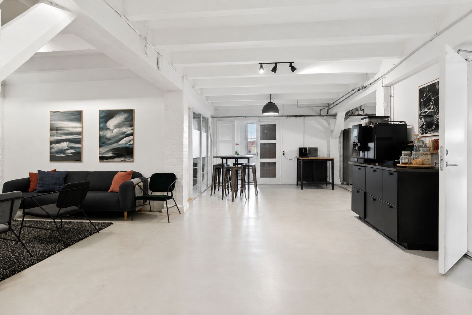 Kontor med højt til loftet, moderne møbler og lyse loftsbjælker i hvidt og stribet loft. Sovesofa med farverige puder og kunstværker i baggrunden.