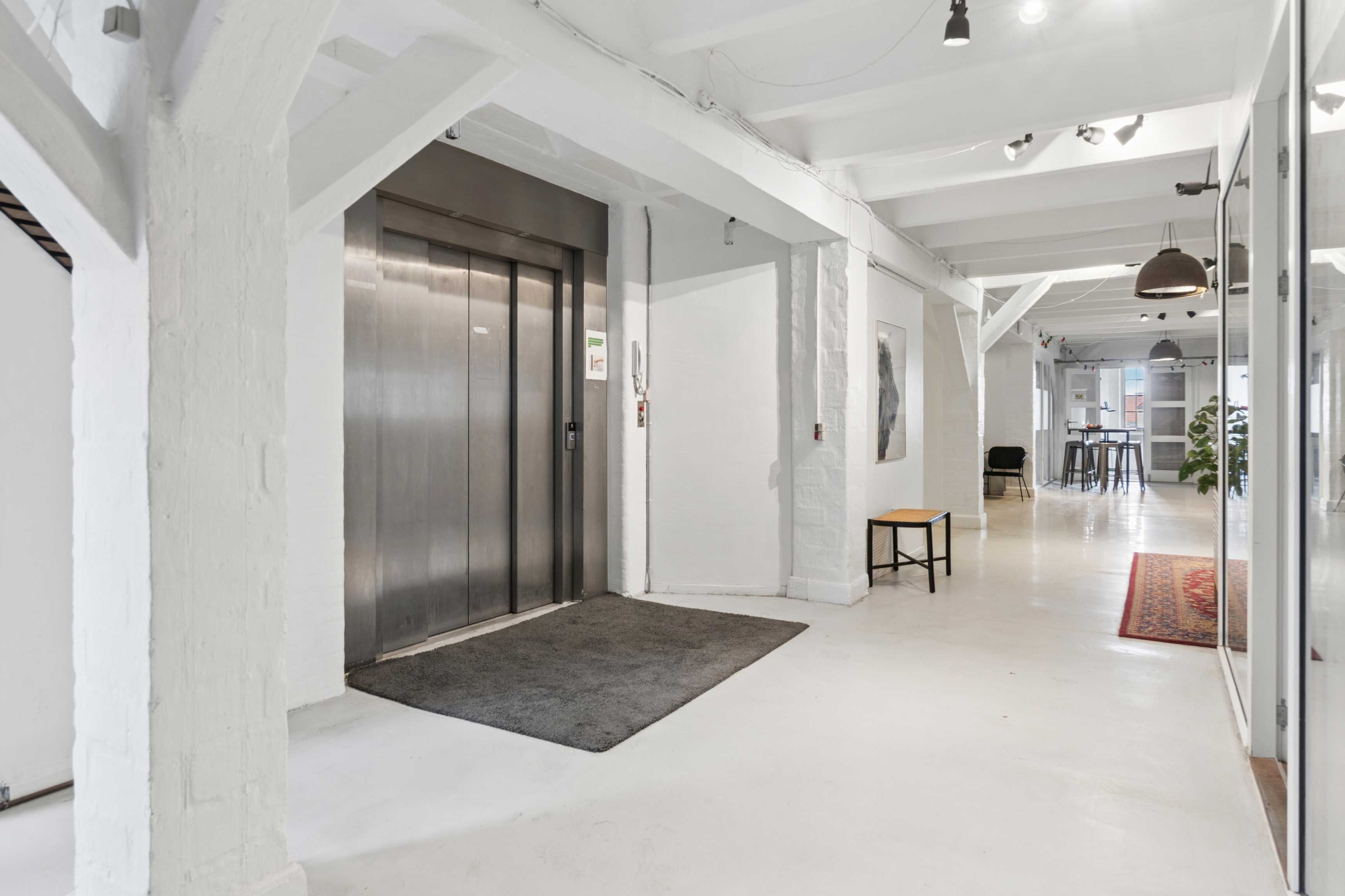 Karakteristisk kontorlejemål med loftsstrukturer og møbleret spisestue, lyse og moderne interiør med møbler og lysekroner, gulvbelægning og dør til elevator.