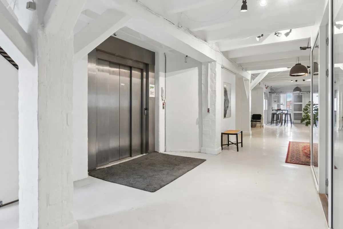 Karakteristisk kontorlejemål med loftsstrukturer og møbleret spisestue, lyse og moderne interiør med møbler og lysekroner, gulvbelægning og dør til elevator.