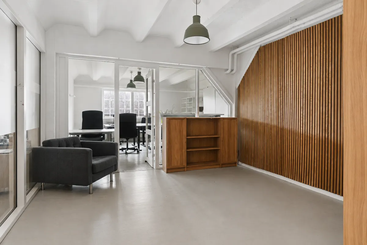 Kontor med lyse lofter, træbeklædte vægge, hvidt interiør, bord, stol og sofa, samt lysekroner og spejl.