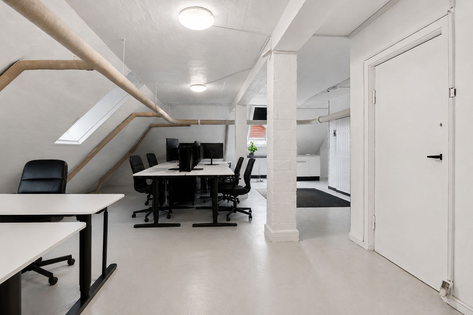 Hvidt kontorlokal med bord og stole i loftsrummet og lysekroner i loftet samt vinduer i loftet og gulvet