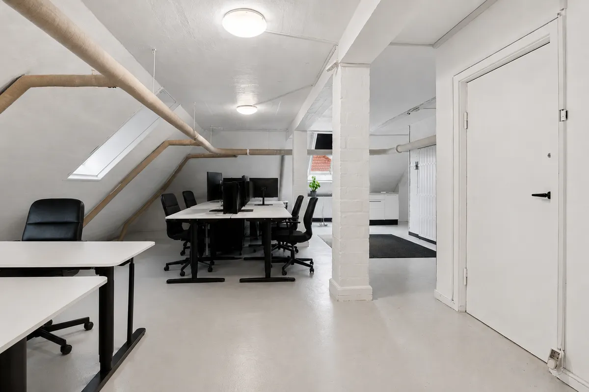 Hvidt kontorlokal med bord og stole i loftsrummet og lysekroner i loftet samt vinduer i loftet og gulvet