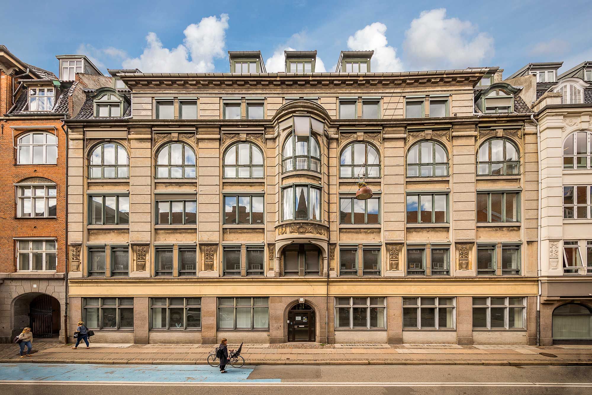 Lyst kontor i klassisk københavnerejendom med udsigt over byens tage og tårne. Bygningen er stor, gammel og har mange vinduer og søjler