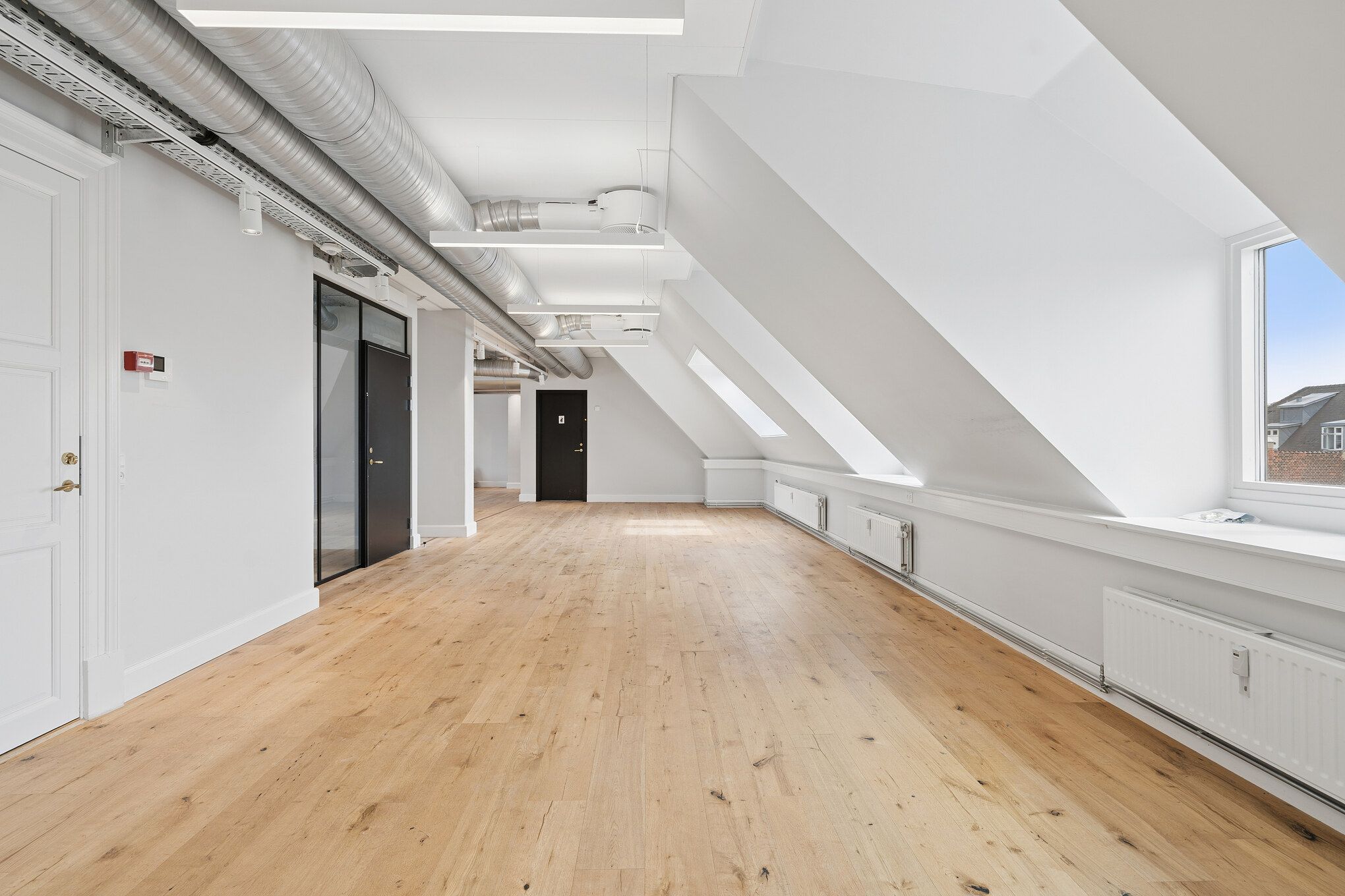 Lyst og charmerende kontor med lyse lofter, hvide vægge og lysegule trægulve. Moderne radiatorer og store vinduer med udsigt over byens tage. Elegante døre og lysekroner.
