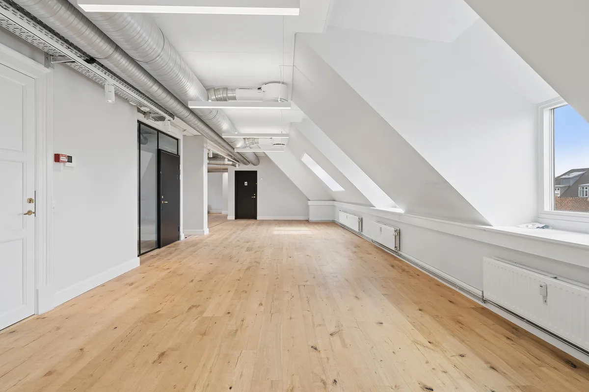 Lyst og charmerende kontor med lyse lofter, hvide vægge og lysegule trægulve. Moderne radiatorer og store vinduer med udsigt over byens tage. Elegante døre og lysekroner.