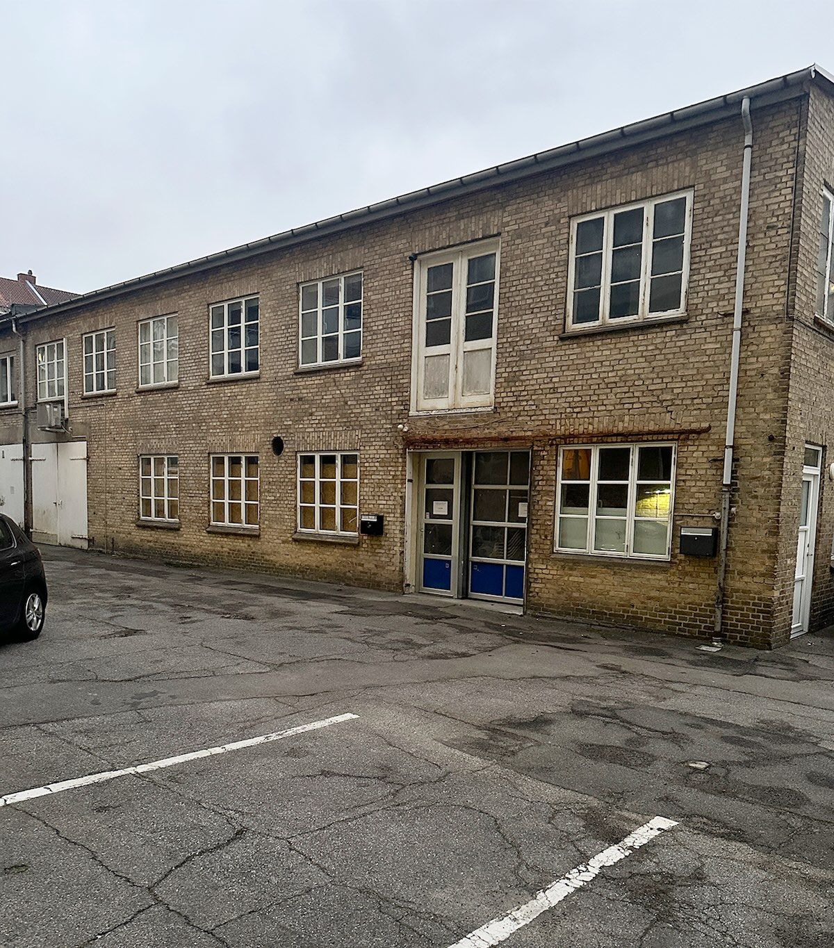 Lejlighed til leje på Fyensgade 34A i Aalborg. Bygningen med røde mursten og hvide vinduerne er placeret i en forstad. Der er to hvide døre og flere vinduer. Et par skraldespande er placeret ved siden af hvert vindue.