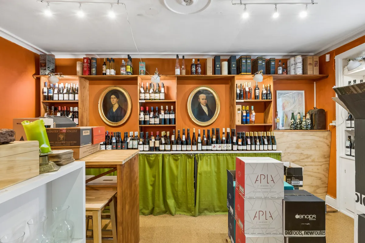 Store hylder med alkohol på butiksloftet. Flasker med etiketten APLÆ står i rækker. Fladskærmstv i loftet og møbler i gulv.
