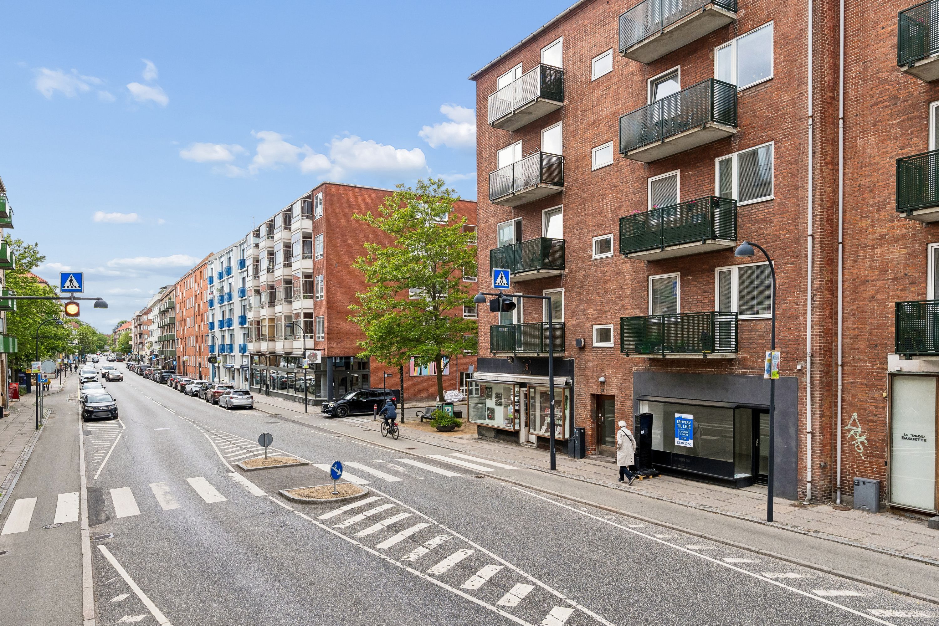 Vejkryds med togskiltet og gåfeltet, forretning med skilt, og biler og cyklister på gågaderne på Ordrupvej i Charlottenlund