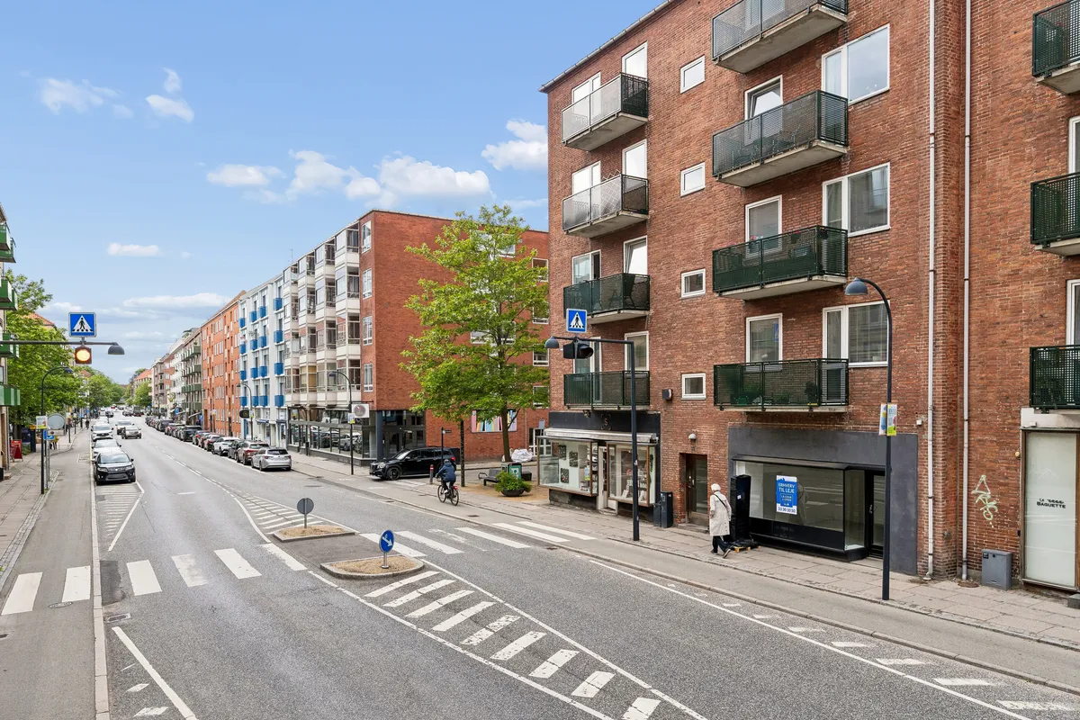 Vejkryds med togskiltet og gåfeltet, forretning med skilt, og biler og cyklister på gågaderne på Ordrupvej i Charlottenlund