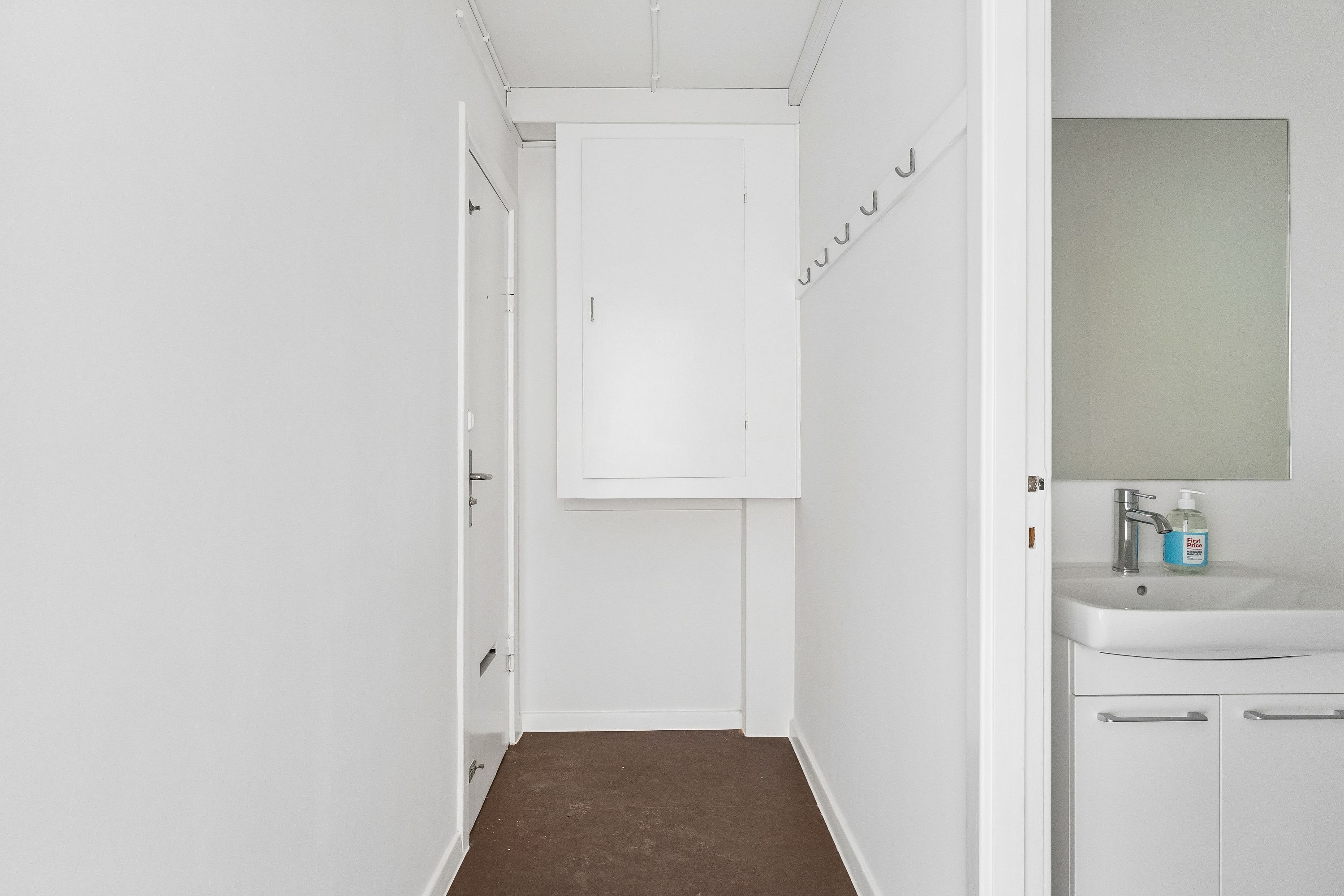 Minimalistisk og rent badeværelse med hvid væg, hvidt håndvask og spejl samt hængegreb og håndklædetørrer