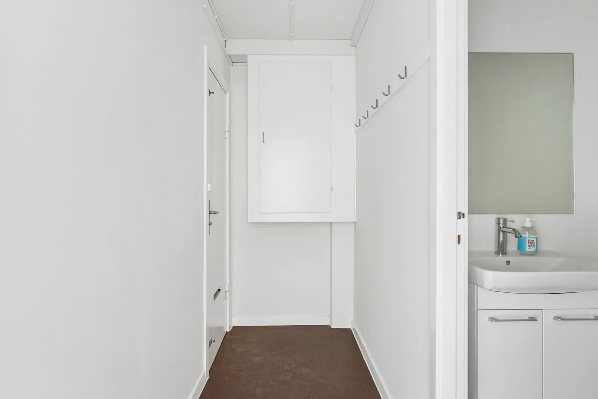 Minimalistisk og rent badeværelse med hvid væg, hvidt håndvask og spejl samt hængegreb og håndklædetørrer