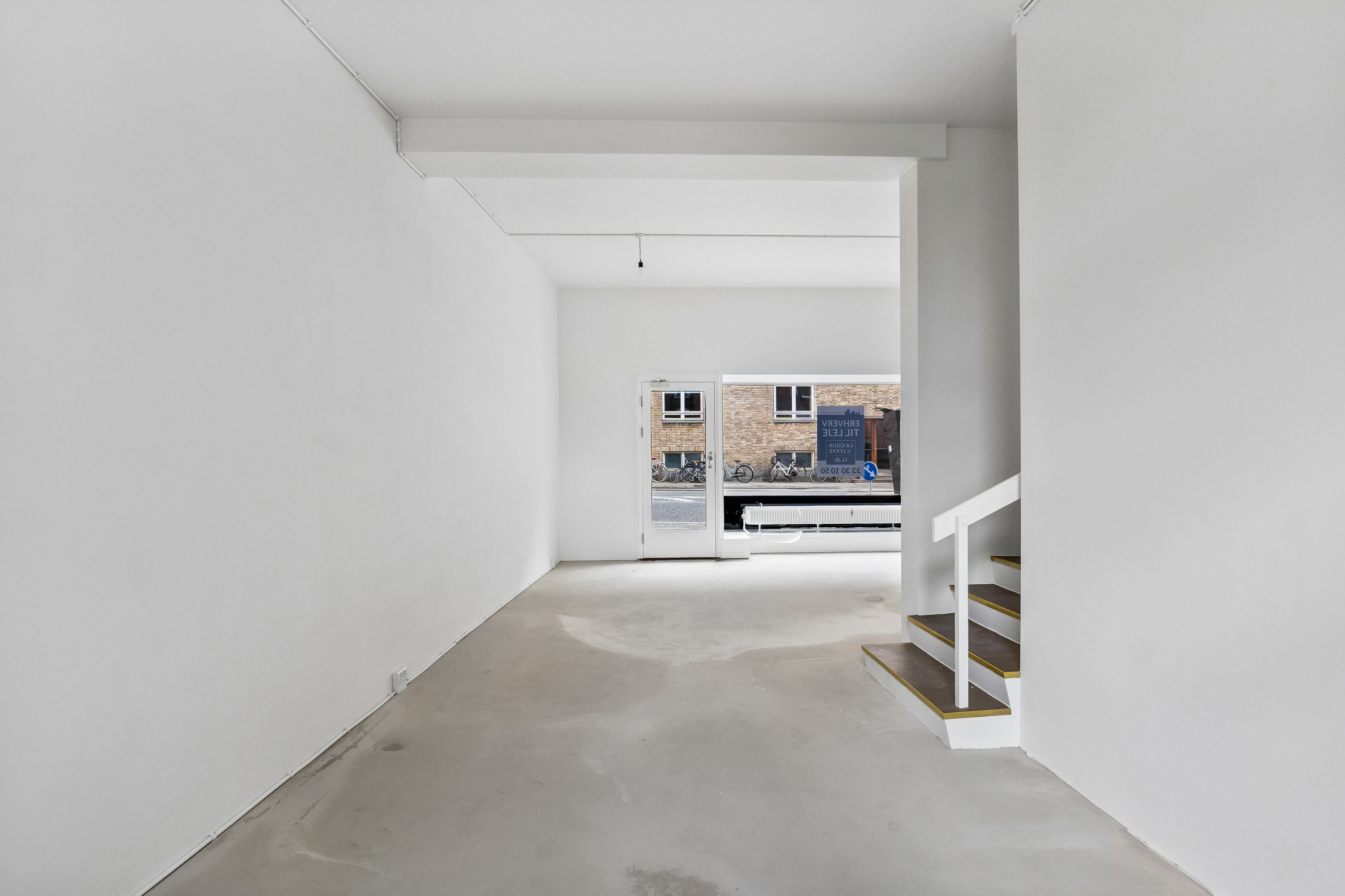 En tom lejlighed med hvide vægge, gulv og loft, hvor der er en åben dør og en trappe til højre