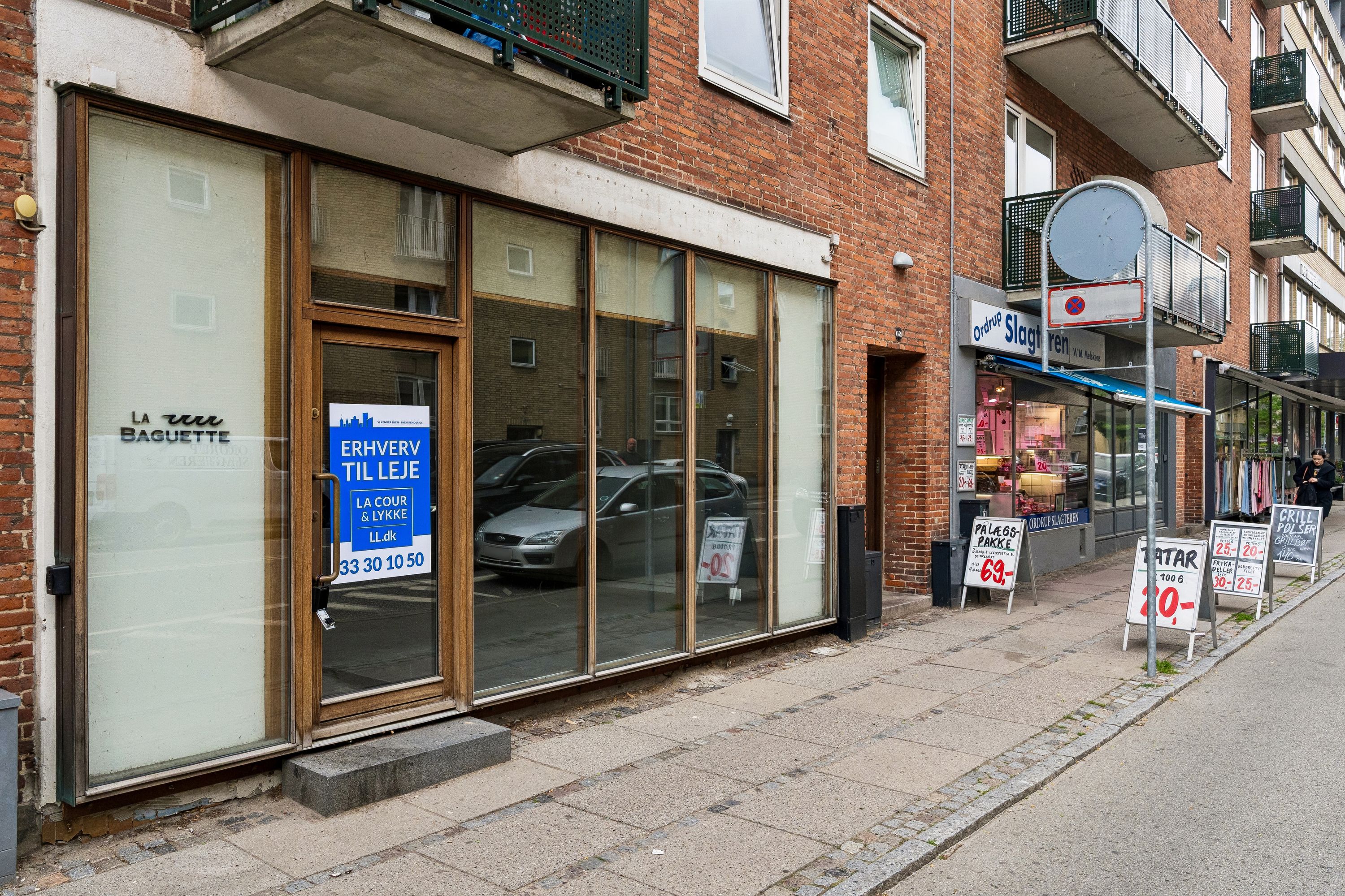 Lejemål til butik på Ordrupvej 62B med skriftligt tekst og reklameskilt, samt en person der går forbi.