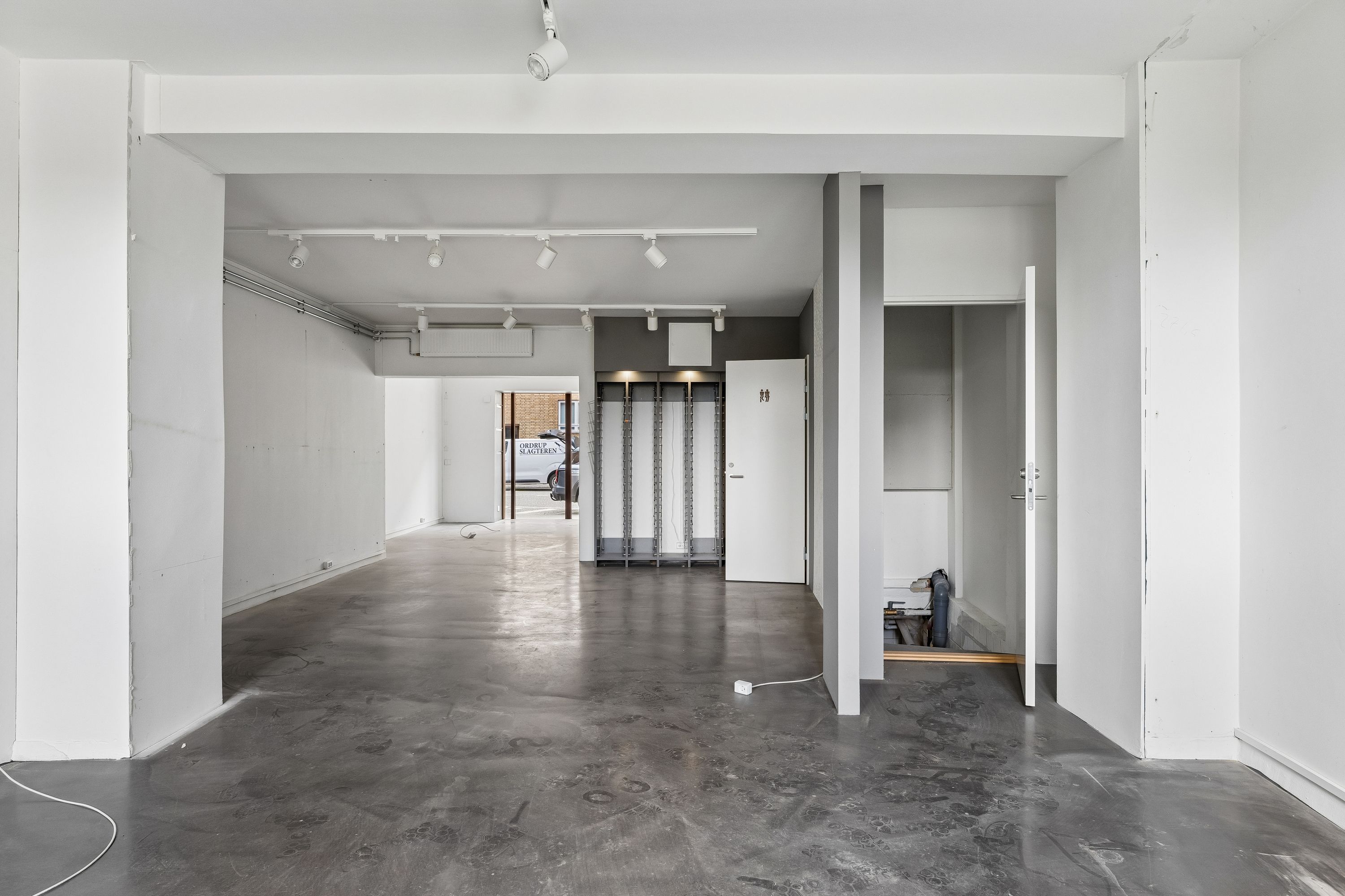 Store tomrum med hvidt loft og gulv samt lysekroner, to døre, kontorrullegardiner og et skur med glasruder og hvide vægge