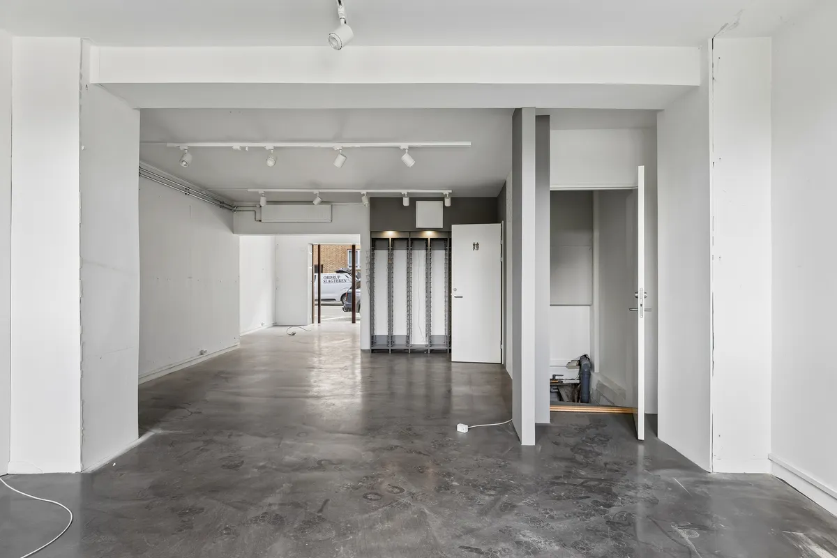 Store tomrum med hvidt loft og gulv samt lysekroner, to døre, kontorrullegardiner og et skur med glasruder og hvide vægge