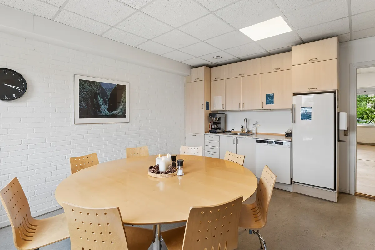 En lyse og moderne møbelfyldt køkkenrum med rundt spisebord og stole samt en lyseblå køleskab og en stor spisestue med en væg med ur og et kunstværk