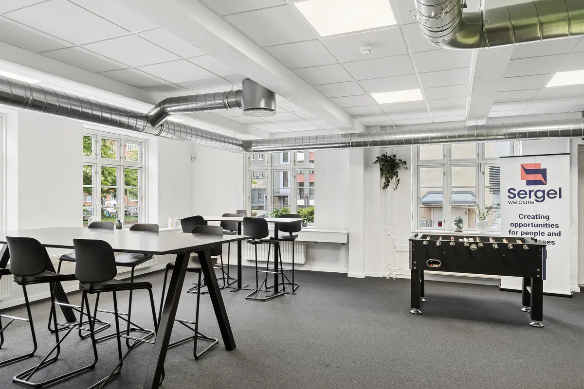 Kontor med store vinduer, højt loft og tekniske faciliteter, fælles kantine og tagterrasse, stolpebord og fodboldbord, smykket med en plante i kassen