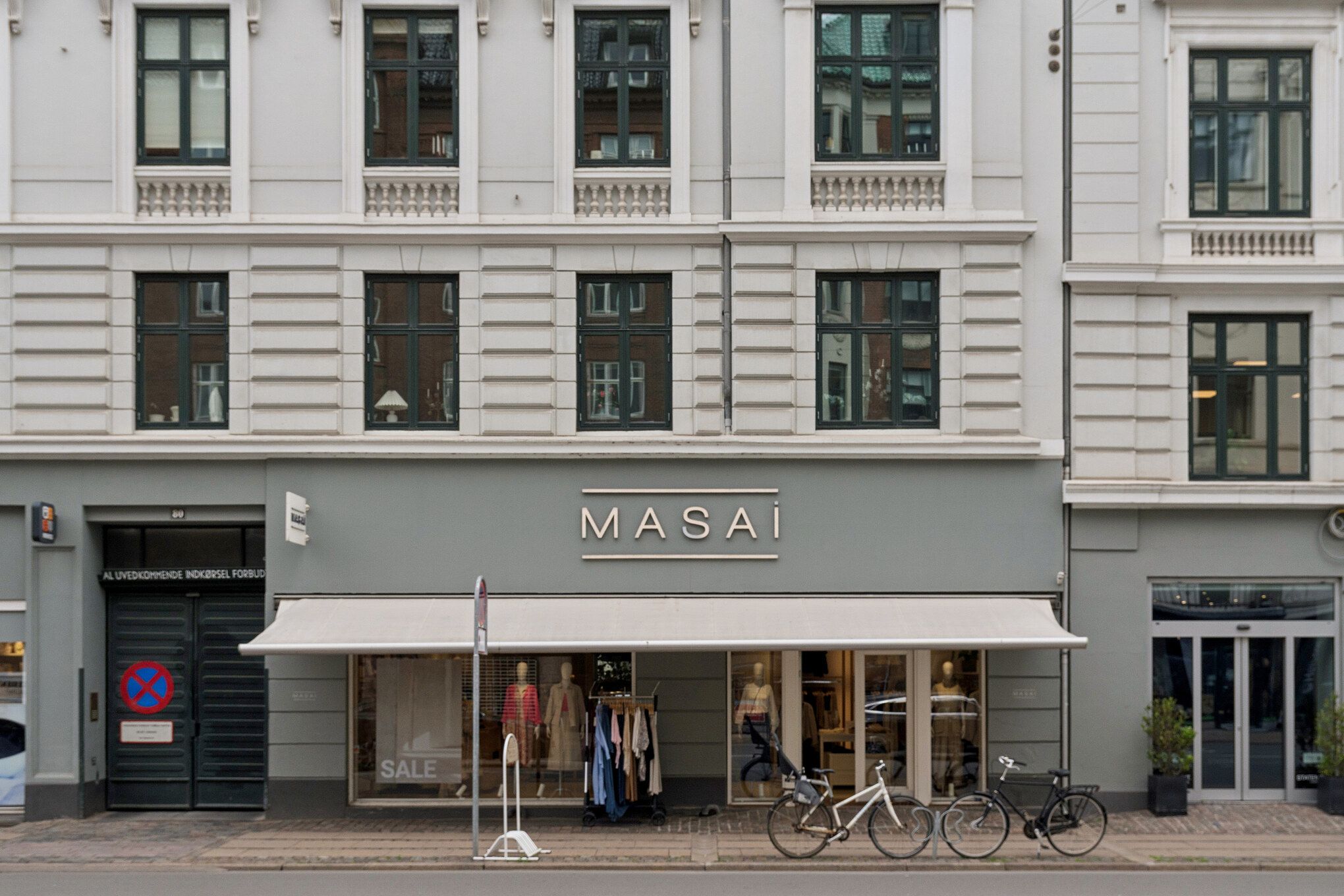 Butikken Masai er placeret i et hjørne og har to cykler parkeret udenfor foran vinduet og en udsalgsskilt