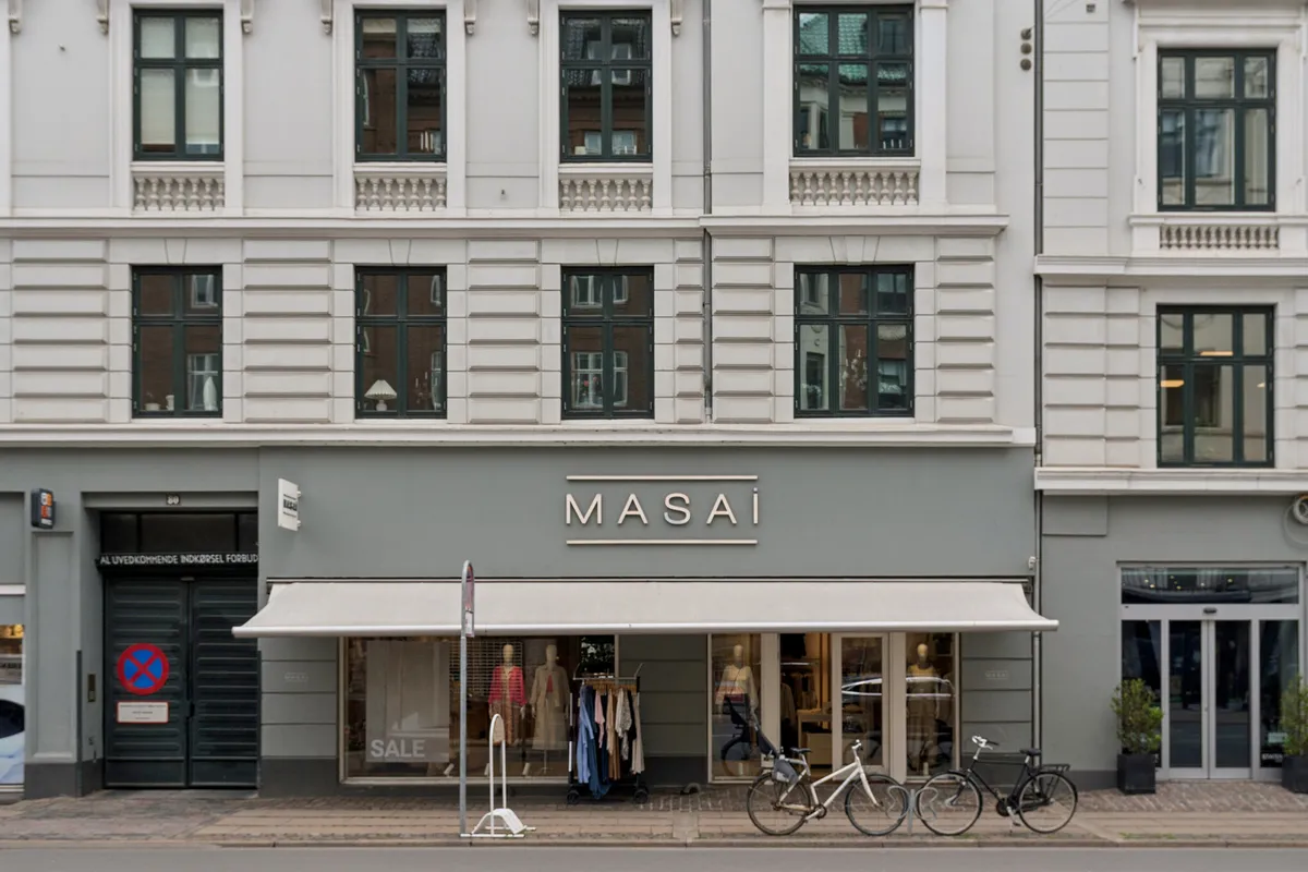 Butikken Masai er placeret i et hjørne og har to cykler parkeret udenfor foran vinduet og en udsalgsskilt