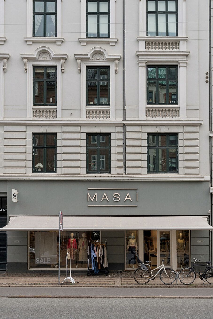 Butik med udsalgsvindue og store ruder med lysegardiner og cykler parkeret udenfor