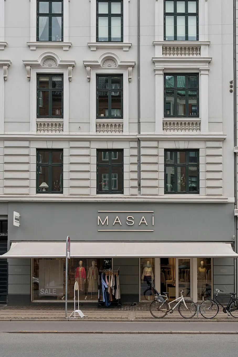 Butik med udsalgsvindue og store ruder med lysegardiner og cykler parkeret udenfor