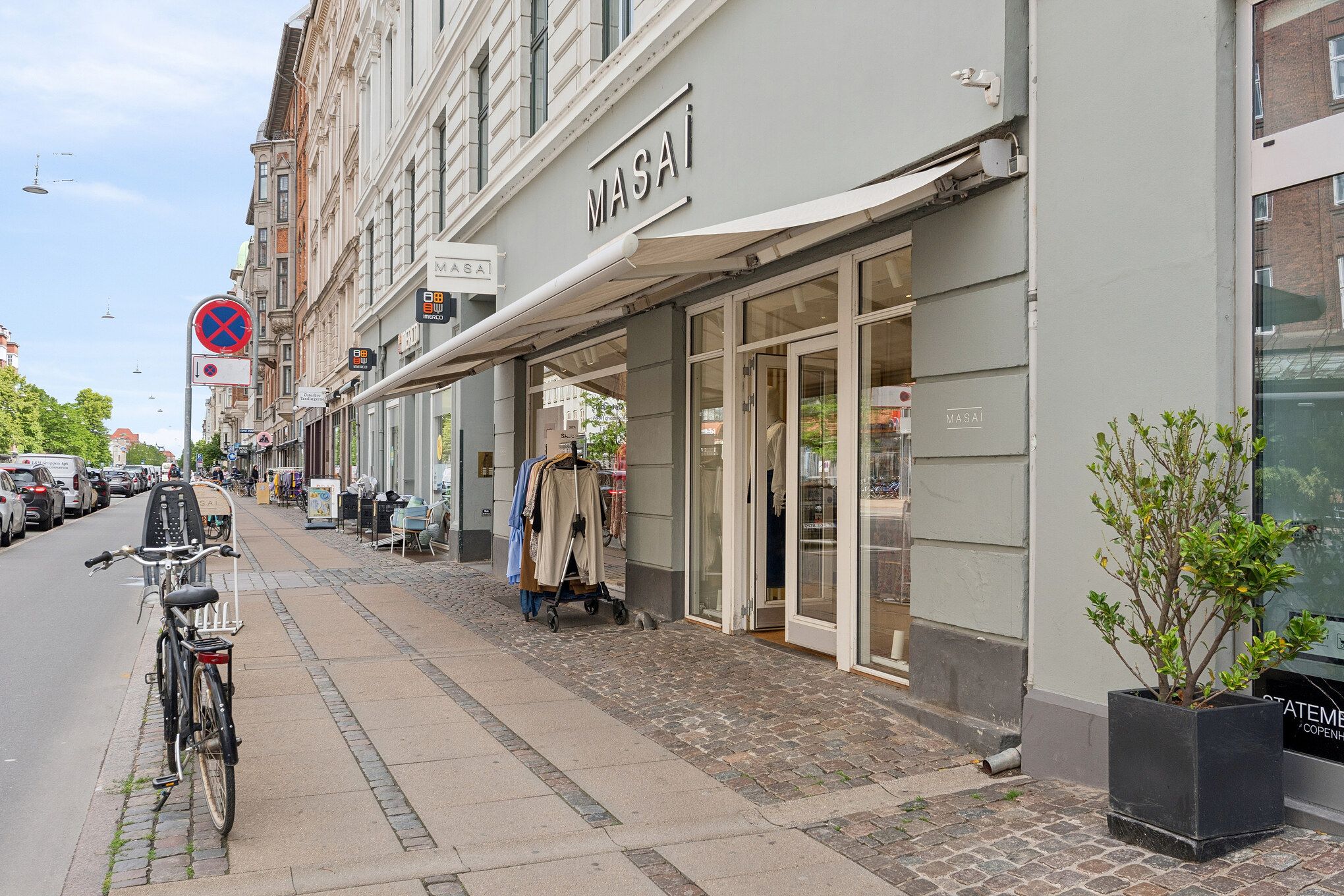 Butik i hjørne med navnet Masa, med klædespind og tøj i udstillingen og cykel og plante foran.