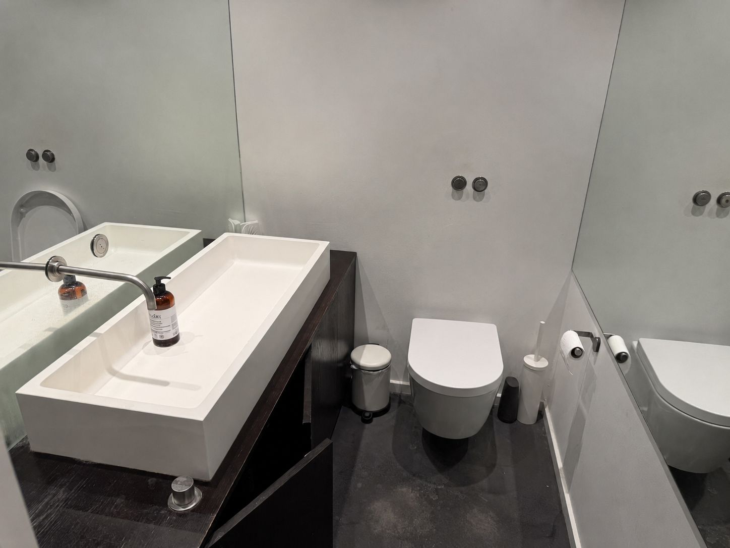 Moderne kontorvand med hvid toilet, dobbelt vask og lysegrå vægge med spejl og toiletpapirholder