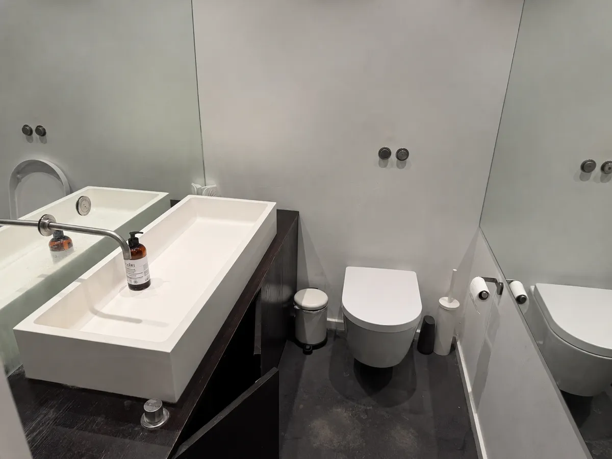 Moderne kontorvand med hvid toilet, dobbelt vask og lysegrå vægge med spejl og toiletpapirholder