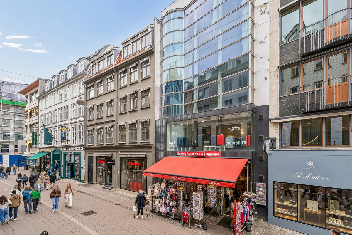Lejlighed på Østergade 10 med moderne møbler og glasvinduer og et stort gulv. Butikker og mennesker er på gaden med forskellige produkter