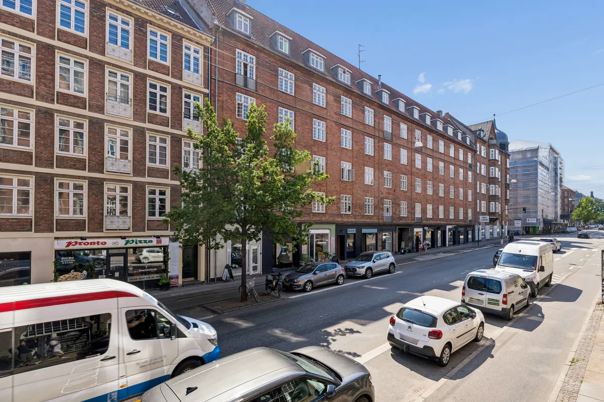 Rækkehus med to butikker og fire lejligheder på Vesterbrogade i Frederiksberg C. En stor bus og en bil er parkeret langs vejen