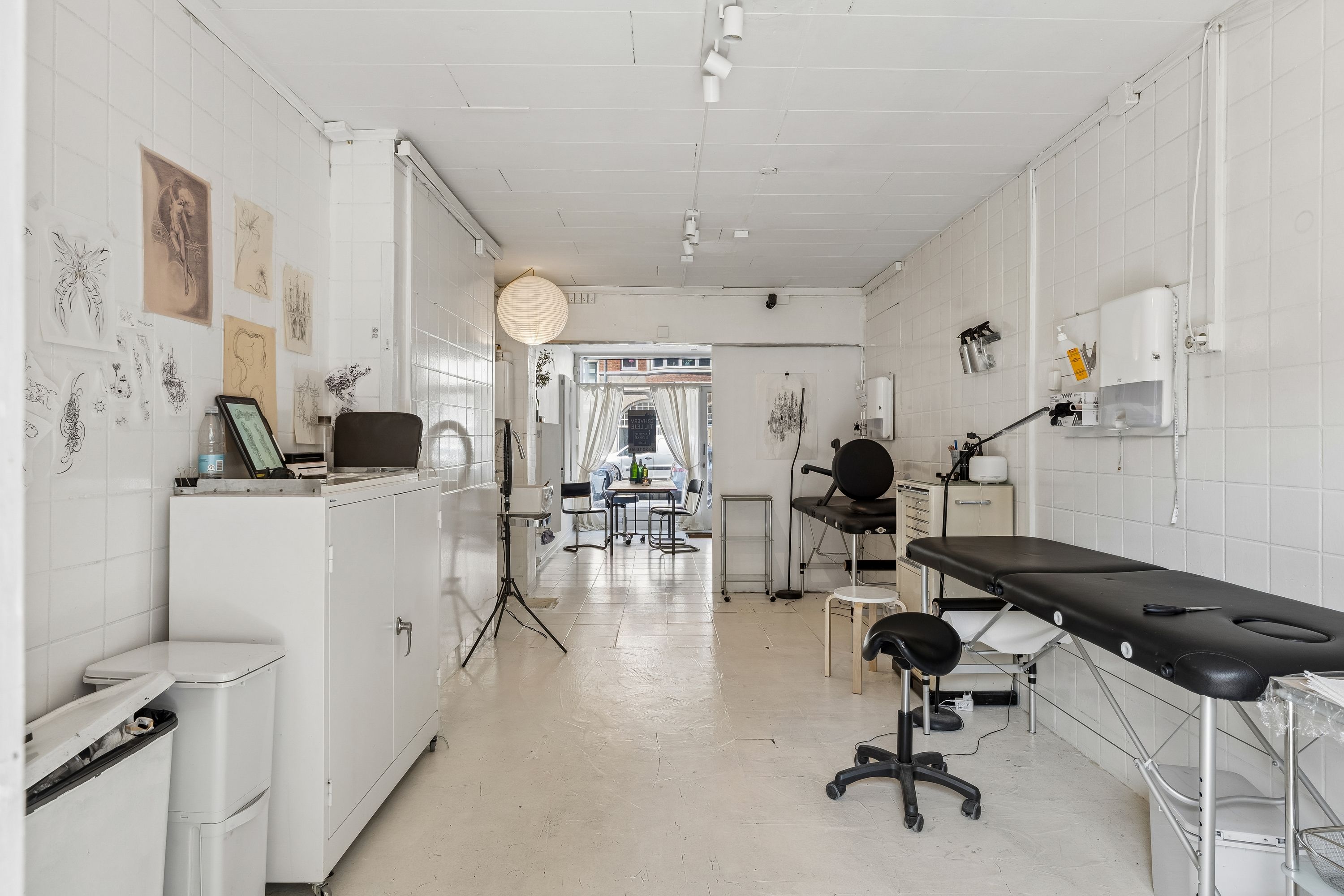 I et lækkert hvidt lokale ser vi en massagebord, en stol, en høj og flere hængte papirer på væggen