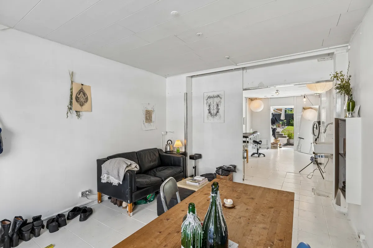 Butikslokal med to store glasruder og indgangsdør, sofa med tæppe, stole og bord med to kølige flasker og krus