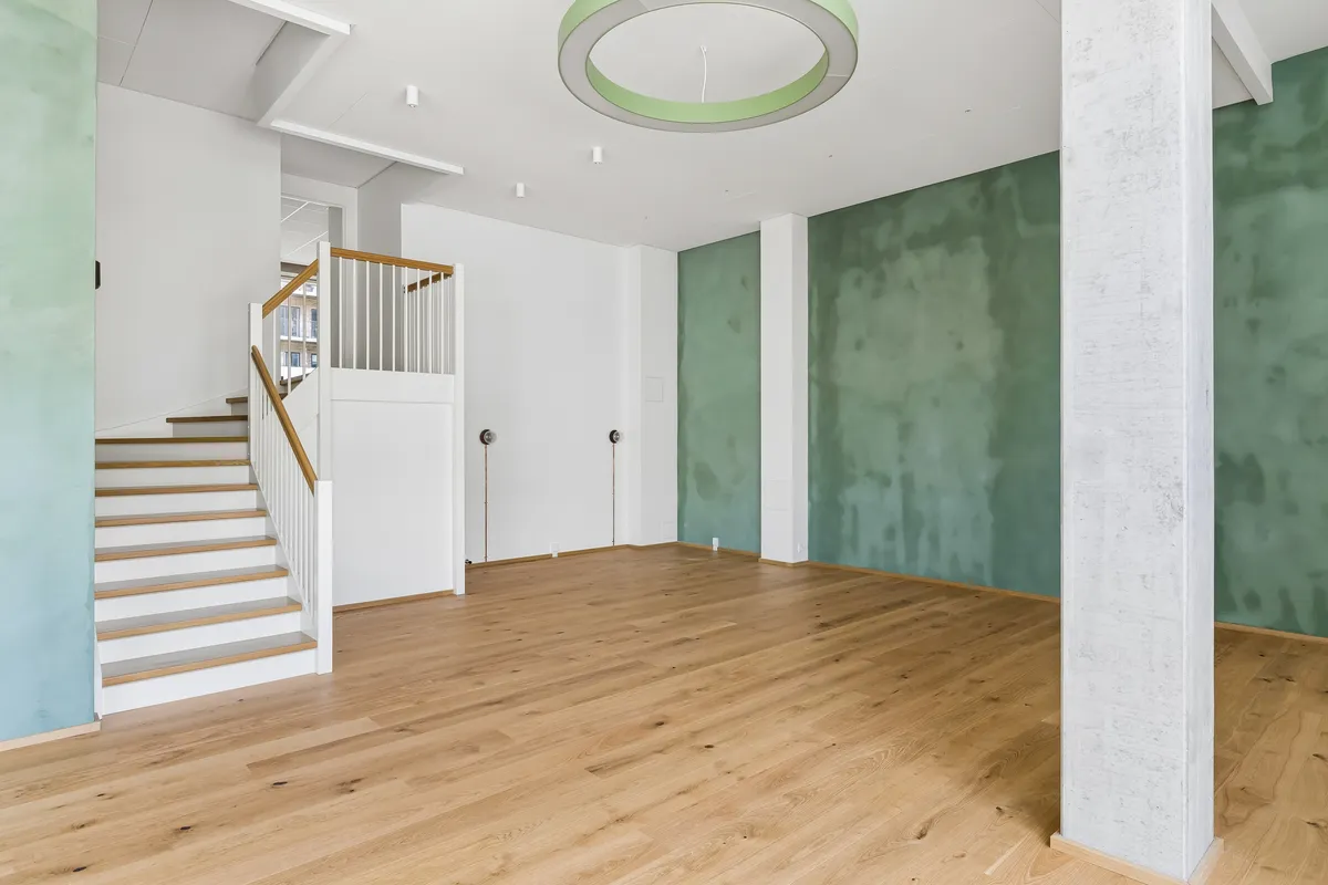 Lyst værelse med højloft og massivt trægulv. Hvid og grøn væg og en lysekron med grøn rand. Stairs med træ og hvidt gelender.