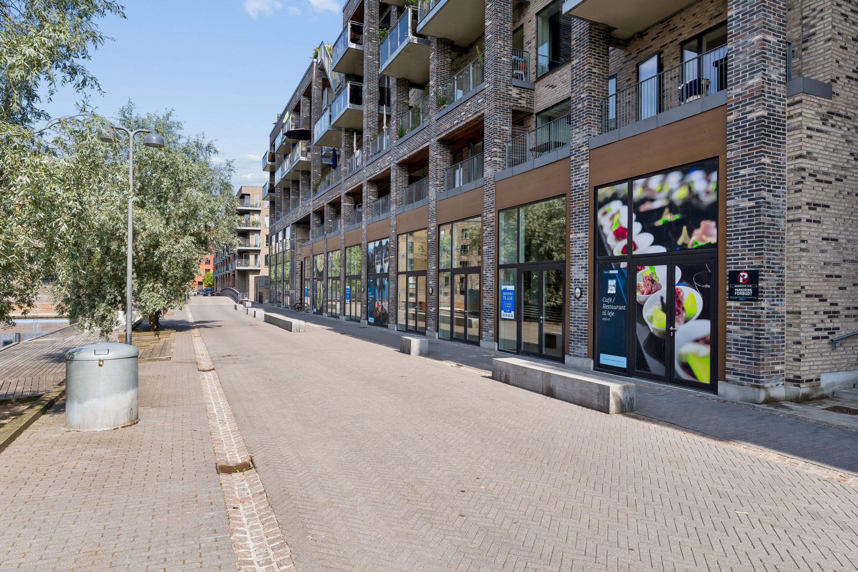 Moderne lejemål med indgangsdør og reklamaner på Lone Kellermanns Vej 23, København SV. Lejlighedsbygning med terrasser og glasvinduer. Lys og rummeligt lejemål.