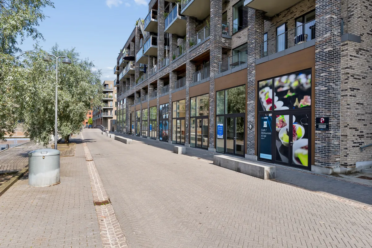 Moderne lejemål med indgangsdør og reklamaner på Lone Kellermanns Vej 23, København SV. Lejlighedsbygning med terrasser og glasvinduer. Lys og rummeligt lejemål.