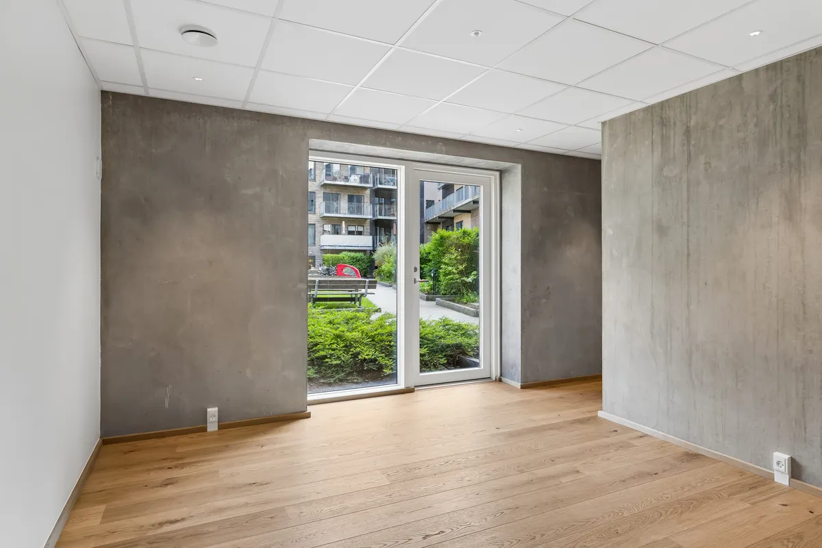 En moderne og lyse lokale med trægulv og hvidt loft, der åbner op mod en terrasse med en række planter og et rød bus.