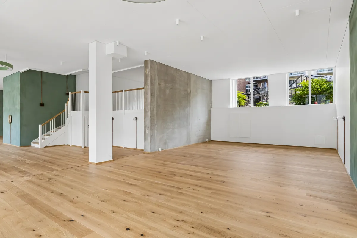 En rummelig og lys lejlighed med hårdt trægulv og lyse loft. Vindueskiltet giver udsigt til grønne træer. En hvid trappe med lyse trin.