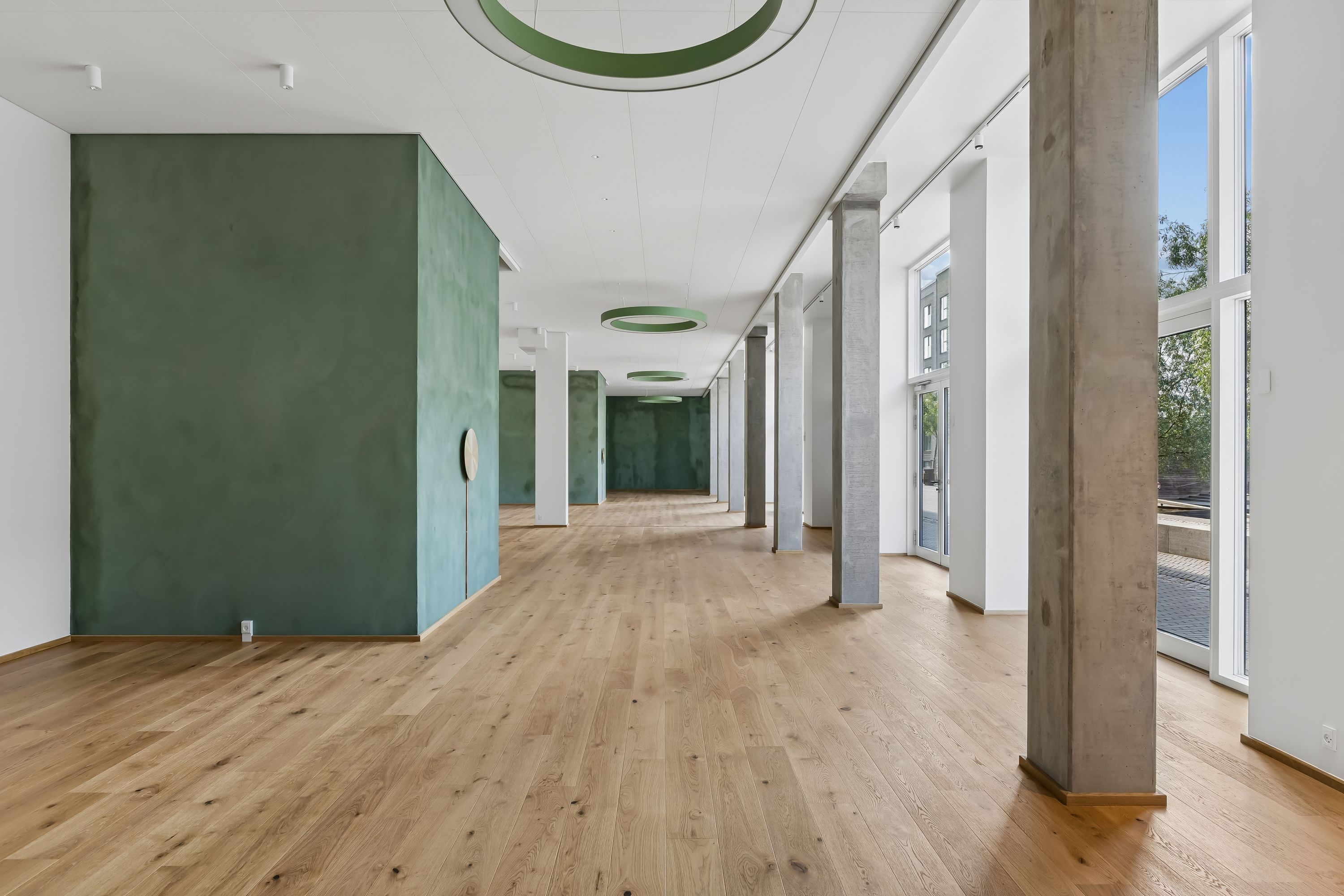 Restaurantlejemål med lyse gulve, smukke lysekroner og grønne vægge. Moderne indretning med tætte søjler og store vinduer. Forskønnede møbler og højt loft.