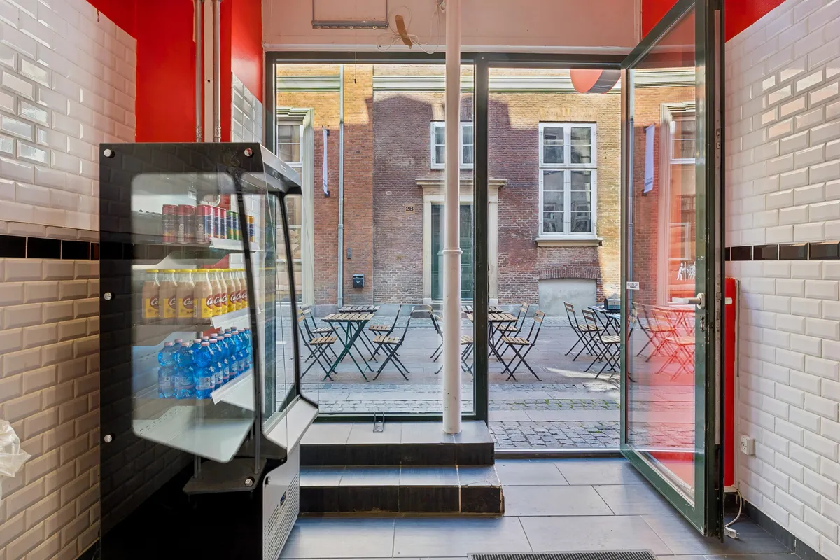 Køkken med tøjde skab og krystallklare ruder, der vender ud mod en terrasse med stole og bord. Mursten og glasvinduer i baggrunden.