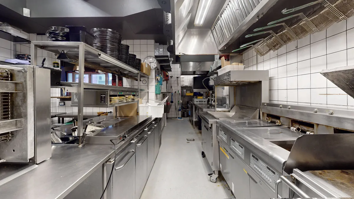 Rummeligt køkken med store rustfritstålapparater og hygiejniske forhold, lyse loftslampe og vinduer med udsigt til gårdhave