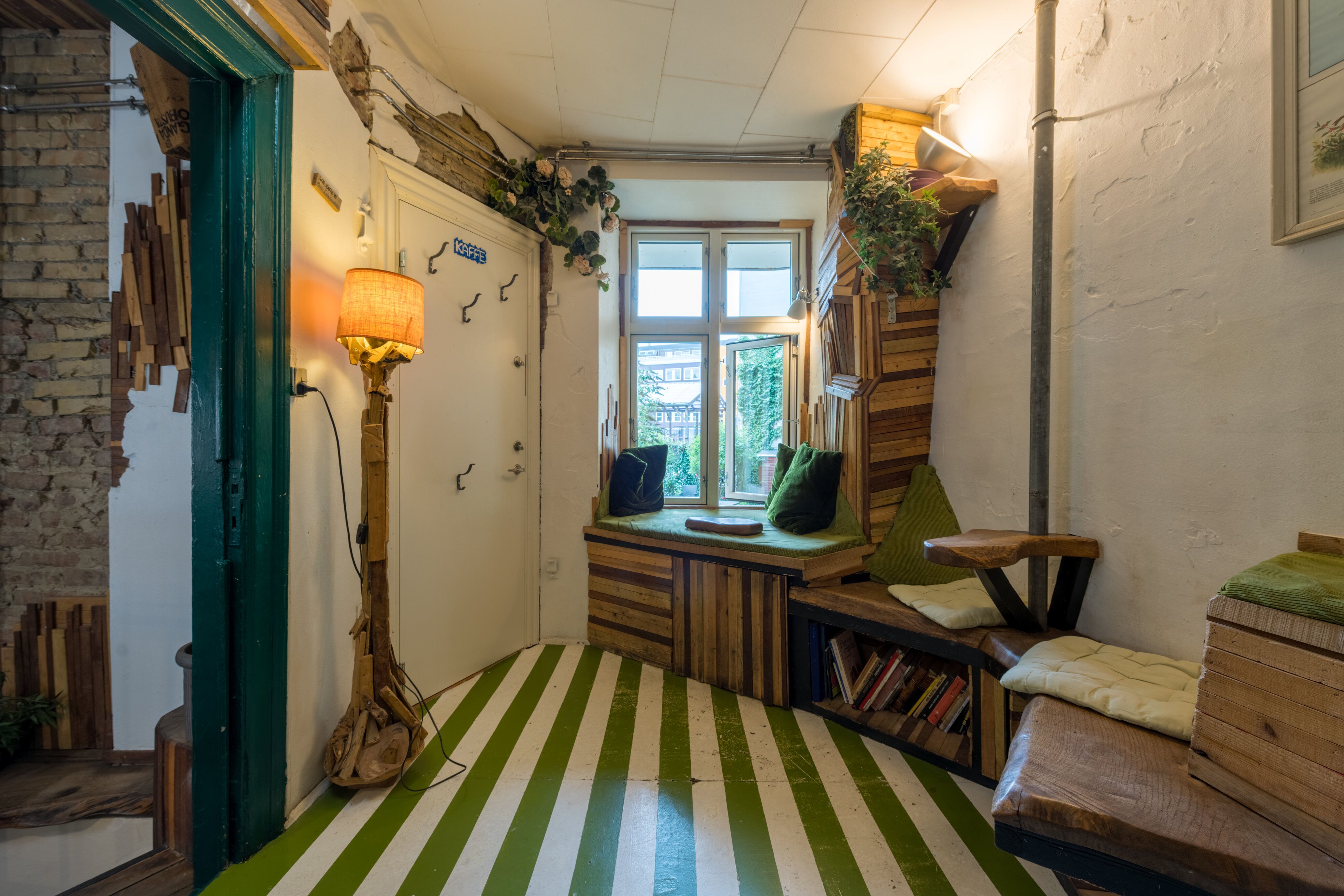 En grøn og hvid stribet gulv og et hyggeligt vinduessiddeplads med grønne puderne og puder samt en lampe i spidsen af rummet