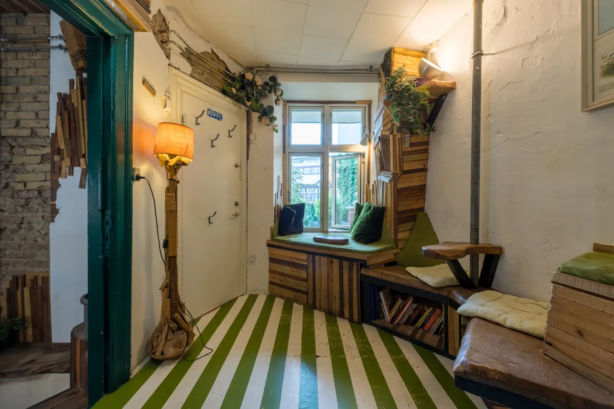 En grøn og hvid stribet gulv og et hyggeligt vinduessiddeplads med grønne puderne og puder samt en lampe i spidsen af rummet