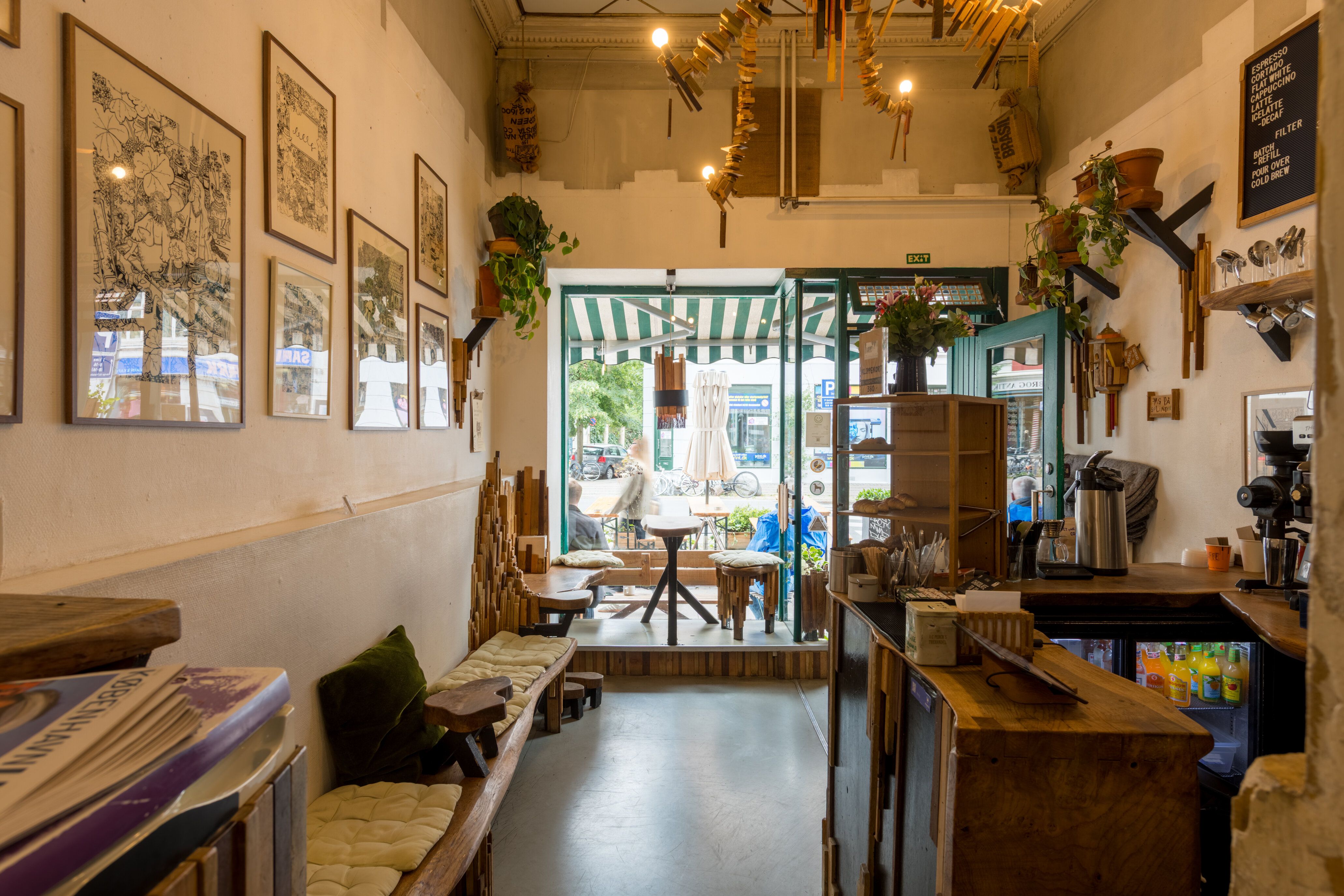 Café med moderne interiør, lyse nuancer og hyggelige sofaer. En træbar, en sofa med pude og et bord med stol. Der er også en stol og et køleskab.