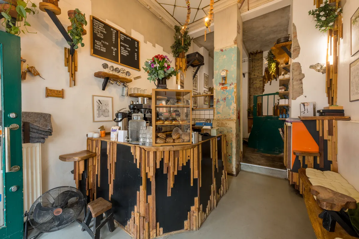 Café med køkken med skrå træ og sort væg og gulv, udskæringer, servietholder, blomster, træhylder, skrifttavle, menu og skrivebord med faner og træstol