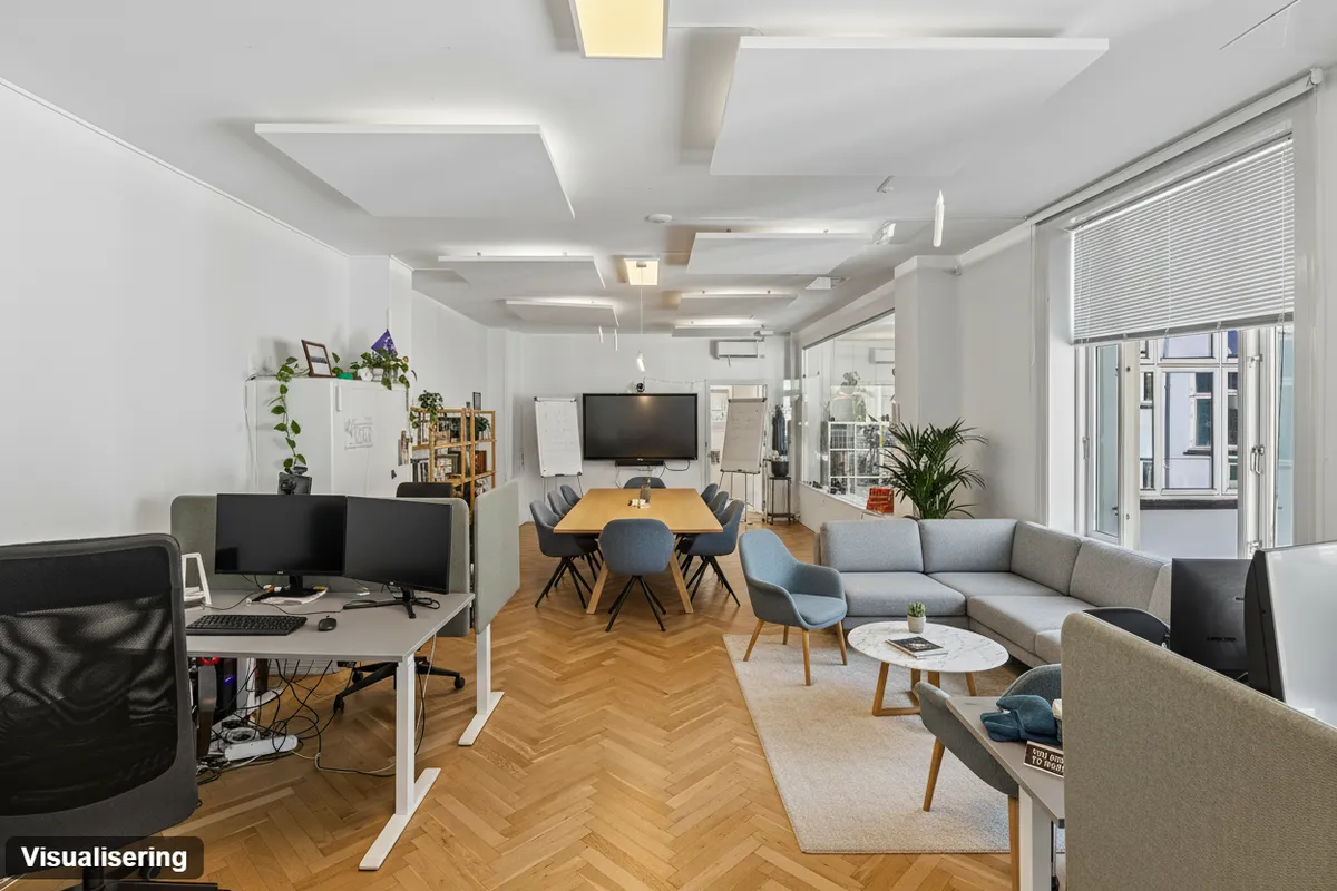 Kontor med højloft og trægulv, skrivebord, monitorer og sofa. Planter og vindue med gardiner. Lyse loftslampe og hvidt loft.